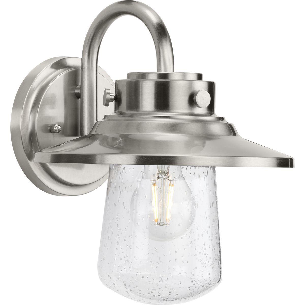 Hubbell P560263-135 Welcome family and friends home with the Tremont Collection 1-Light Clear Seeded Glass Stainless Steel Industrial Outdoor Medium Wall Lantern Light. A light source glows from within a clear seeded glass shade reminiscent of raindrops on a window after a s