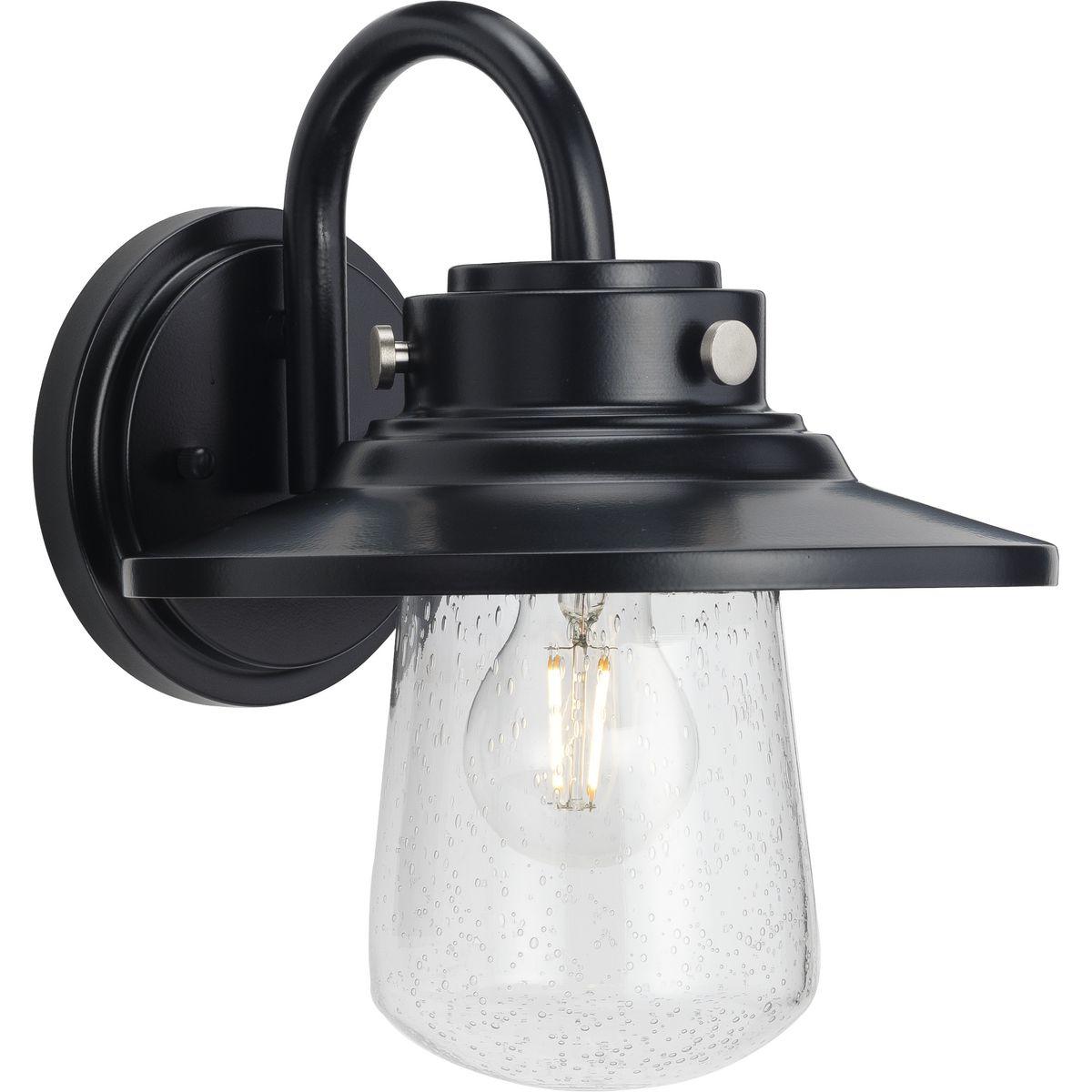 Hubbell P560263-031 Welcome family and friends home with the Tremont Collection 1-Light Clear Seeded Glass Matte Black Industrial Outdoor Medium Wall Lantern Light. A light source glows from within a clear seeded glass shade reminiscent of raindrops on a window after a summe